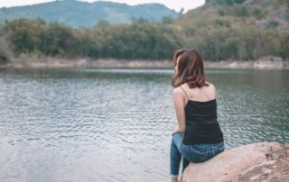 Woman sitting on rock looking at water